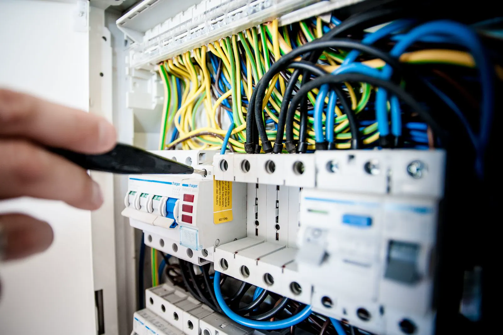 Illustrative photo of a hand working among coloured wires in an open switchboard. Not an A1 Electricians job.